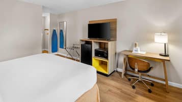 Een hotelkamer met een bed, een bureau met een computer, een televisie, een lamp en een stoel.