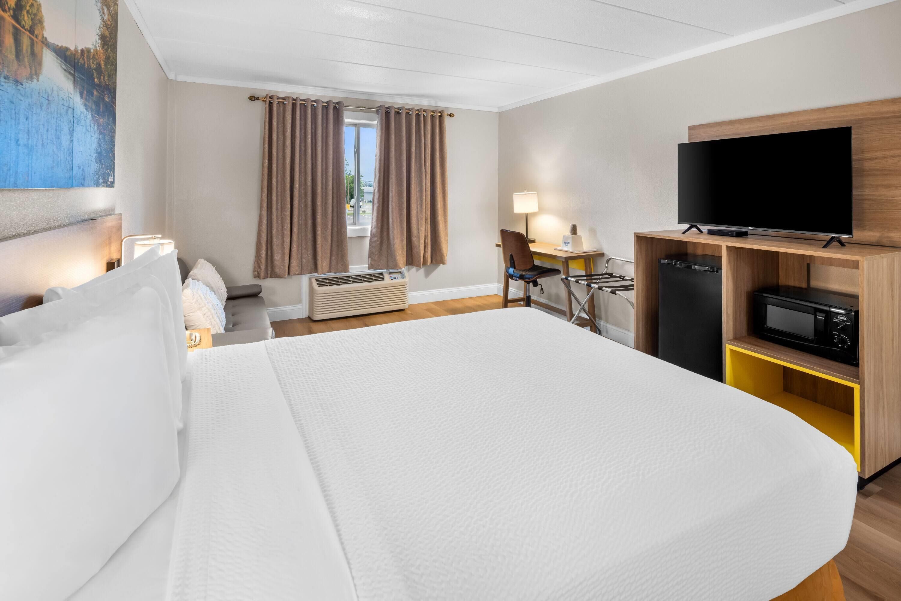 Habitación de hotel con una cama grande, un escritorio con una silla, un televisor y un microondas.