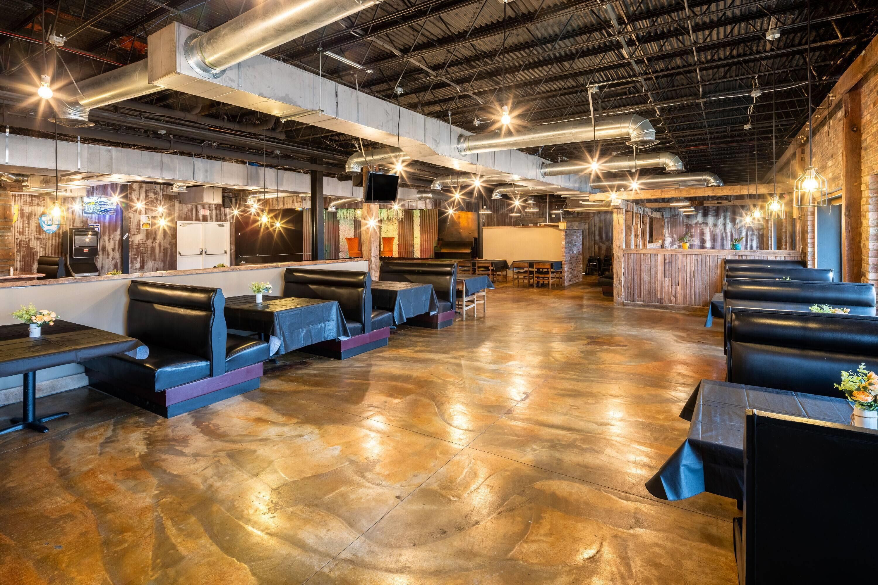 A spacious indoor dining area with booths and tables, exposed ductwork, and a brick wall.