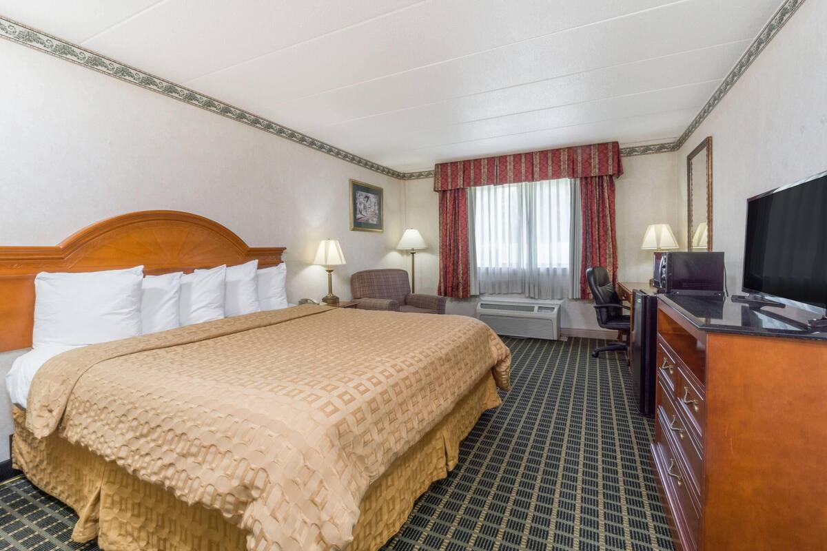 A hotel room with a large bed, a desk, a chair, a television, and a window with curtains.