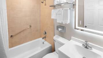Un baño moderno con bañera, inodoro y lavabo. Hay un perchero con toallas, un cabezal de ducha y un dispensador de papel higiénico.