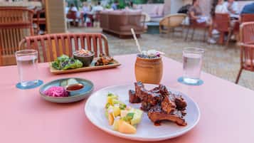 An outdoor dining area with a pink table, plates of food, and a rustic wooden pot.
