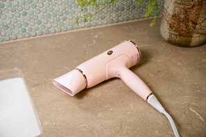 A pink hair dryer on a textured countertop with a tiled backsplash and a potted plant.