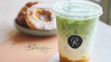 A beverage in a clear plastic cup with a logo, and a plate with a pastry in the background.