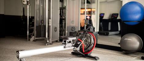 Un vélo d’appartement dans une salle de sport, avec des ballons d’exercice et des appareils de musculation en arrière-plan.