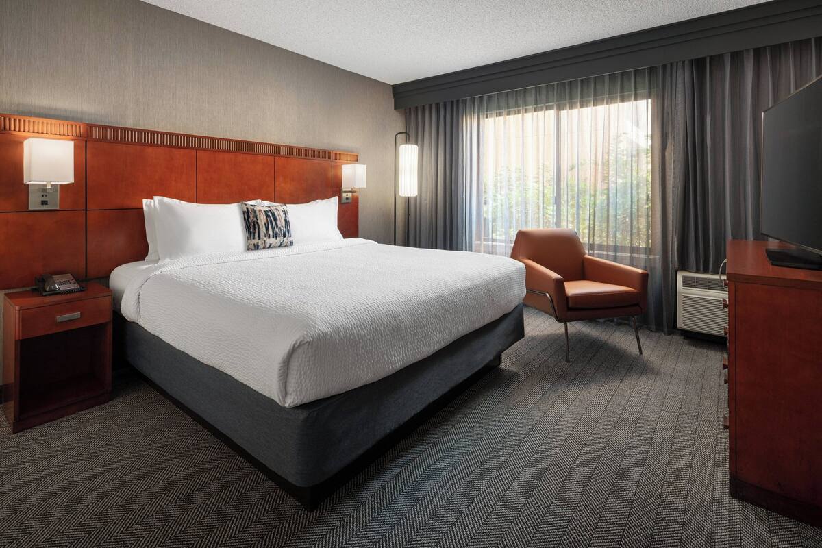 Ein Hotelzimmer mit einem großen Bett, einem Sessel, einem Schreibtisch und einem Fernseher.