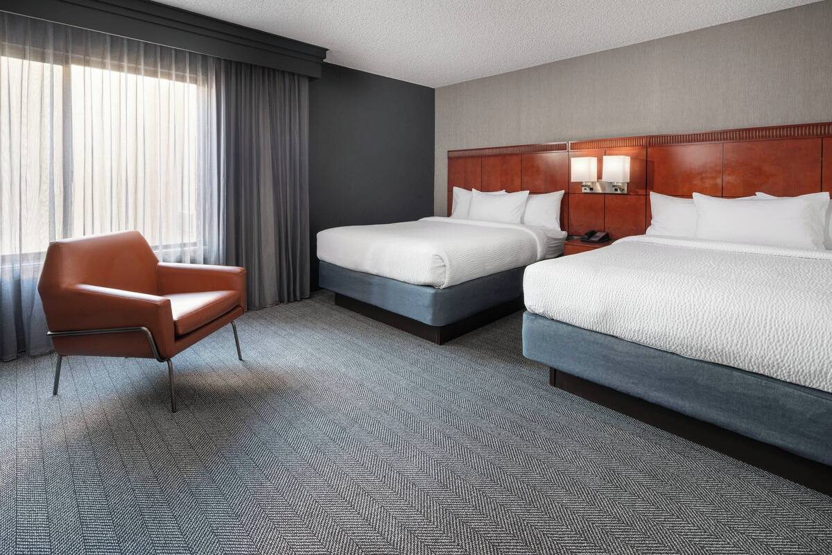 Ein Hotelzimmer mit zwei Betten, einem Sessel und einem großen Fenster mit Vorhängen.