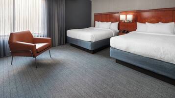 A hotel room with two beds, a chair, and a large window with curtains.