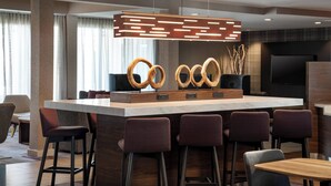 Un espace bar moderne doté d’un îlot central, de tabourets de bar et d’un luminaire suspendu original.