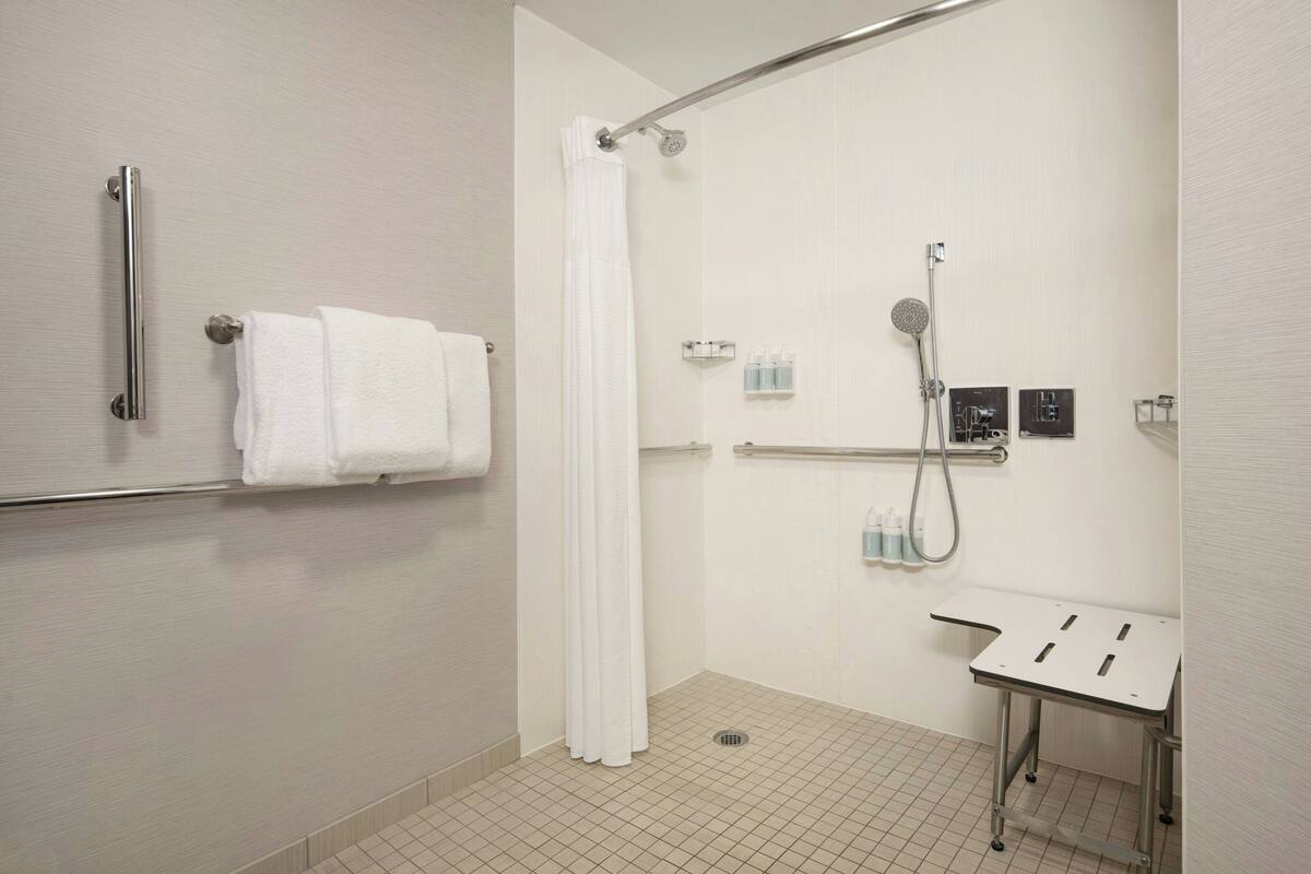 Ein modernes Badezimmer mit Dusche, Haltegriffen, einem Handtuchhalter und einem kleinen Waschbecken.
