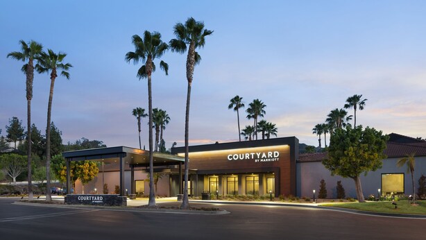 Un hôtel Courtyard by Marriott doté d’une façade moderne, de palmiers et d’une entrée bien éclairée.
