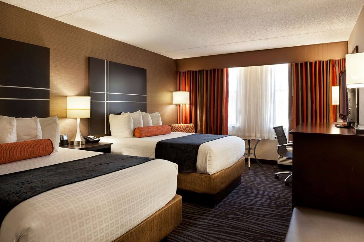 Une chambre d’hôtel avec deux lits, un bureau, une chaise et une grande fenêtre avec des rideaux.