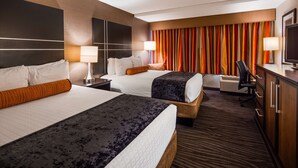 Ein Hotelzimmer mit zwei Betten, einem Schreibtisch, einem Sessel, einem Fernseher und einem großen Fenster mit Vorhängen.