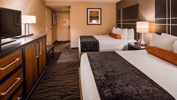 A hotel room with two beds, a TV, a desk, and a lamp.