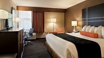 A hotel room with a large bed, a desk with a chair, a television, and a window with curtains.