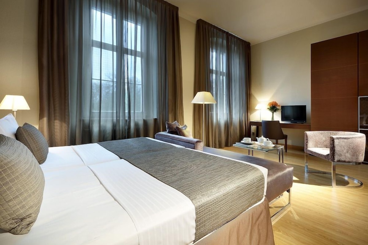 Habitación de hotel con una cama grande, dos mesitas de noche, un televisor, un escritorio con una silla y un sofá.
