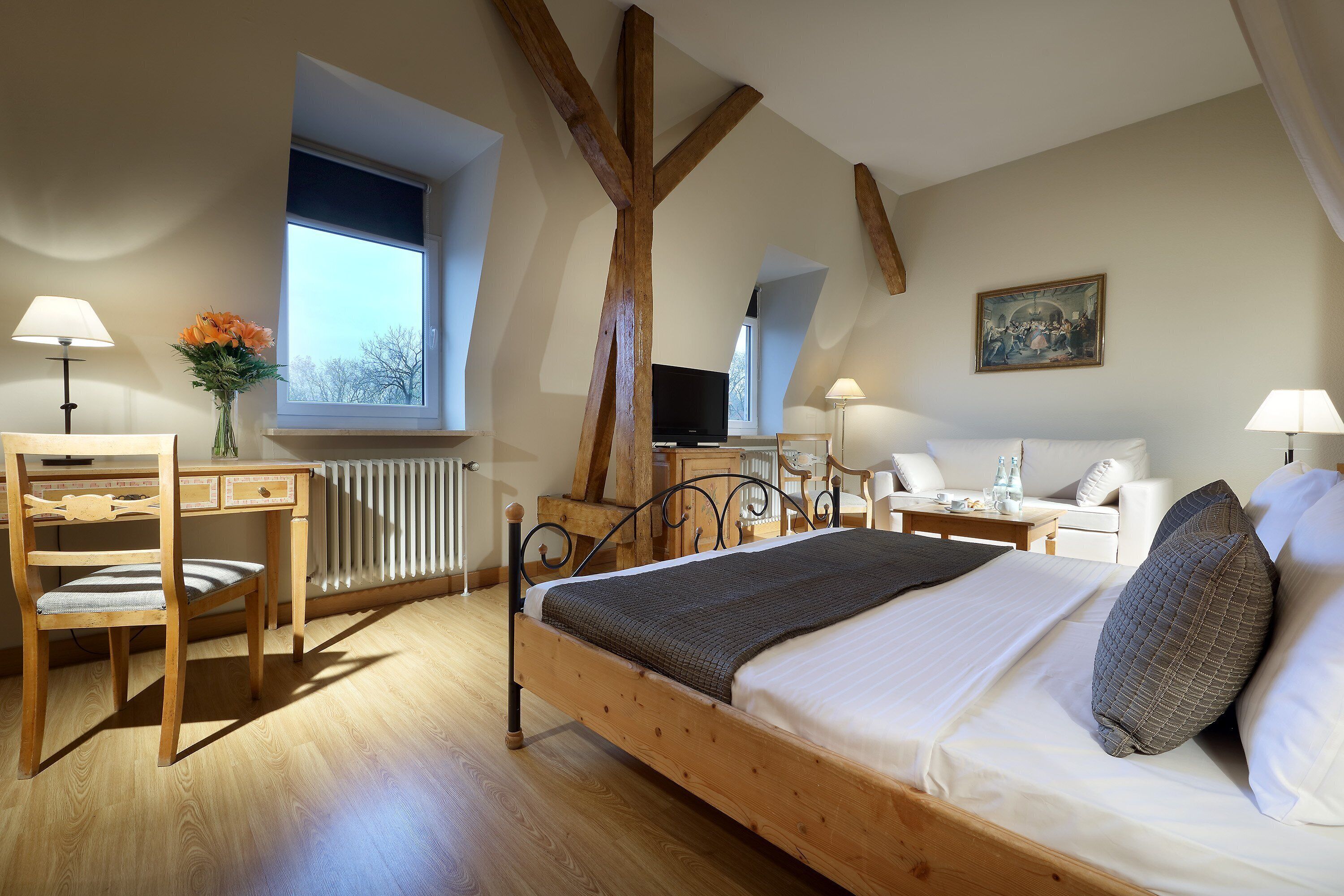 Een slaapkamer met een houten bed, een bureau, een stoel, een radiator, een raam en een schilderij aan de muur.