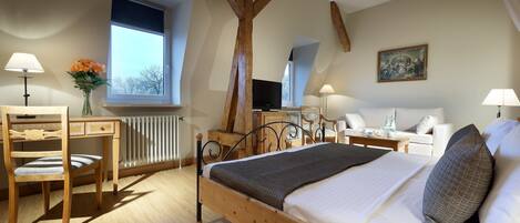 Een slaapkamer met een houten bed, een bureau, een stoel, een radiator, een raam en een schilderij aan de muur.