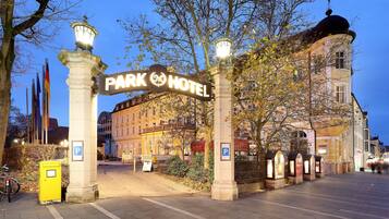 A hotel entrance with a sign reading "Park Hotel," a parking sign, and a lamp post.