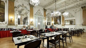 Un amplio salón comedor con elaboradas decoraciones en el techo, candelabros y una zona de bufé cubierta con manteles rojos.