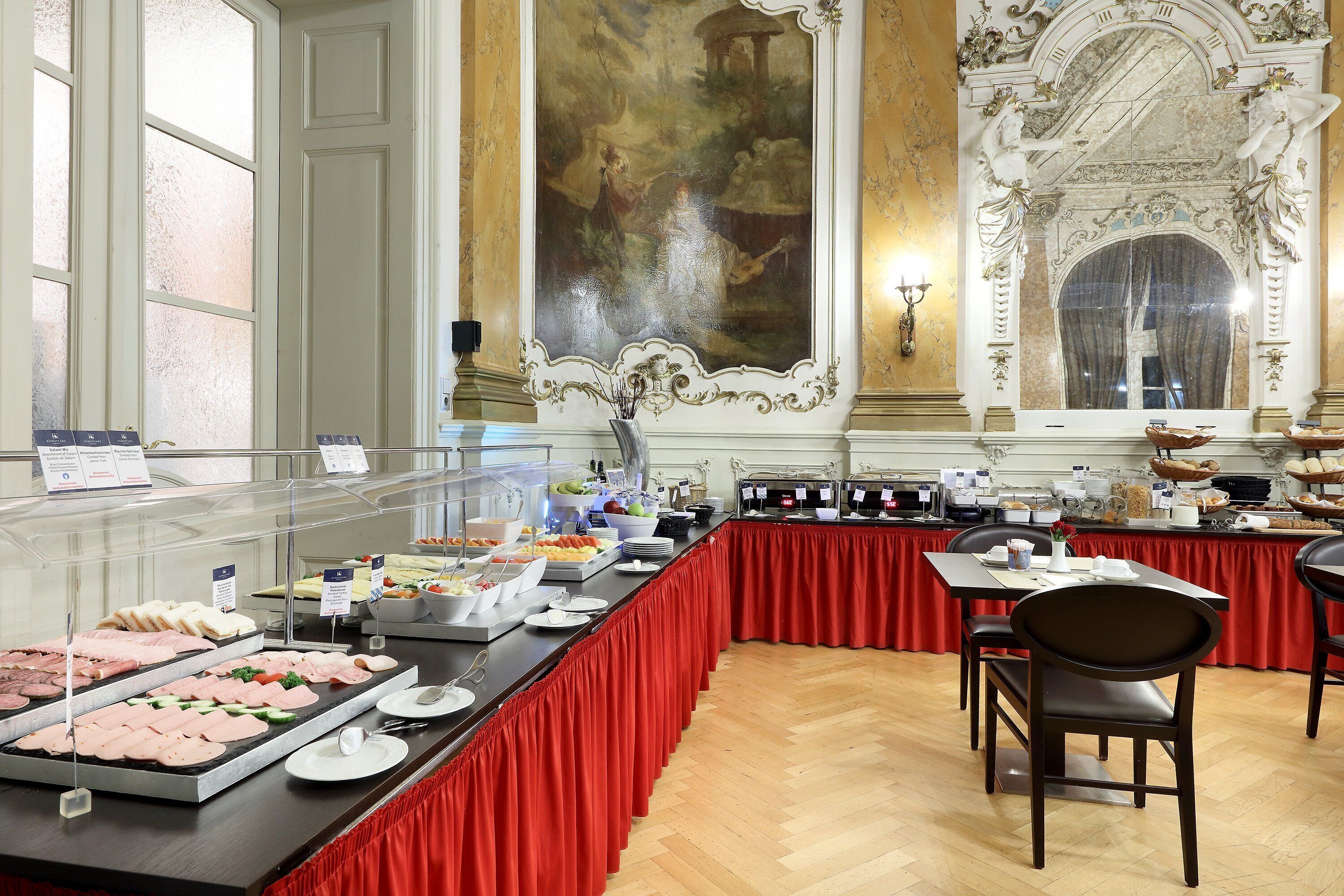 Een buffetopstelling met diverse gerechten en een groot decoratief schilderij aan de muur.