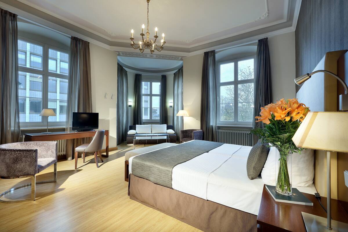 Una habitación de hotel con una cama grande, un escritorio con silla, un televisor y un florero con flores.