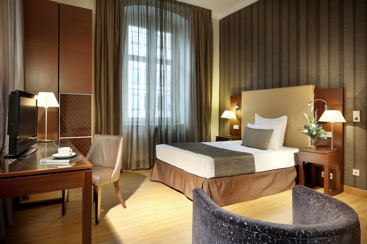 Una habitación de hotel con una cama, un escritorio con una silla, un televisor y dos lámparas.