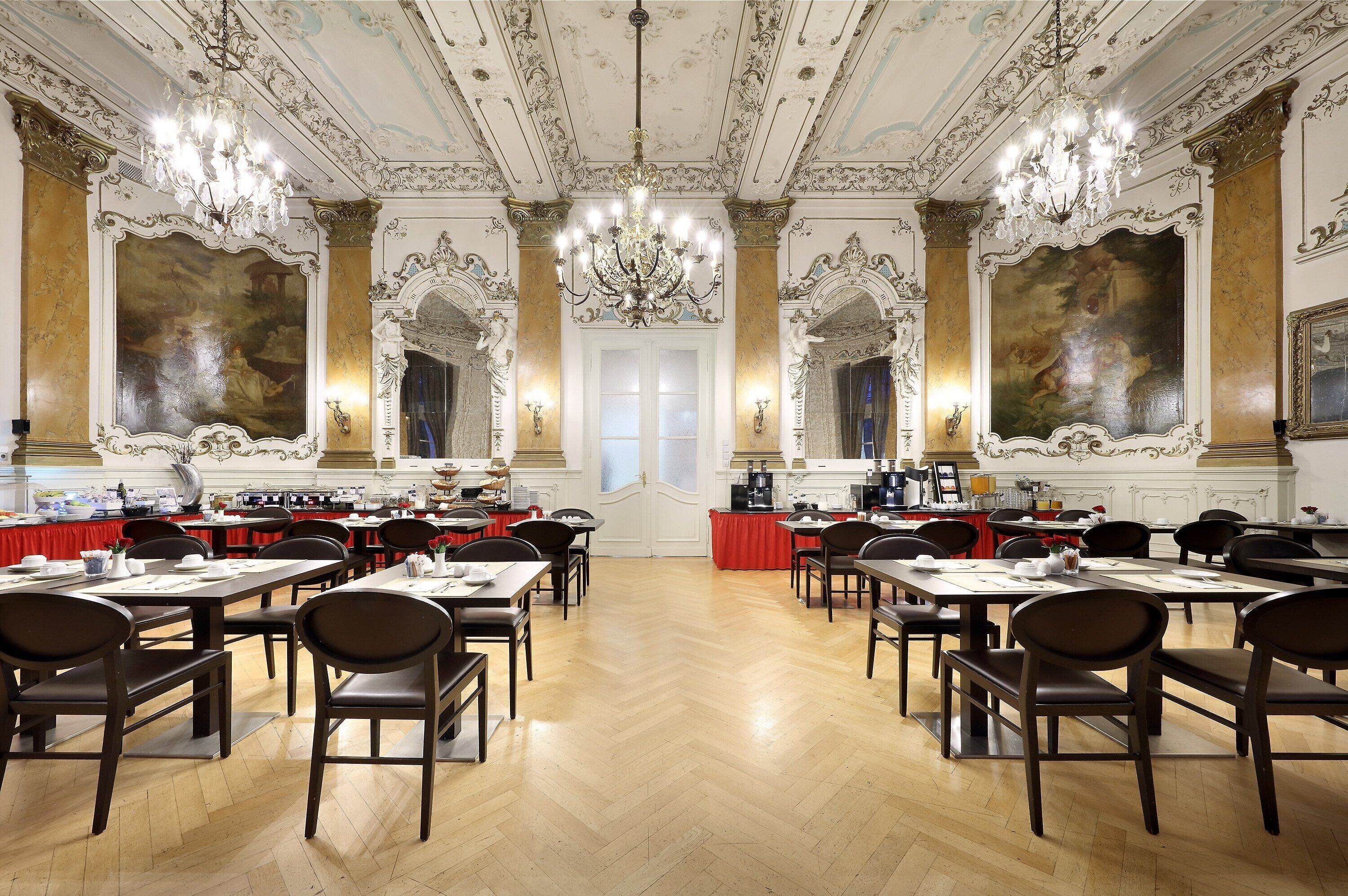 A grand banquet hall with ornate chandeliers, high ceilings, and elaborate wall paintings. Tables are set for a formal event.