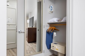 Une chambre d’hôtel équipée d’un placard, d’un miroir, d’une télévision, d’une étagère avec des serviettes et d’un étendoir.