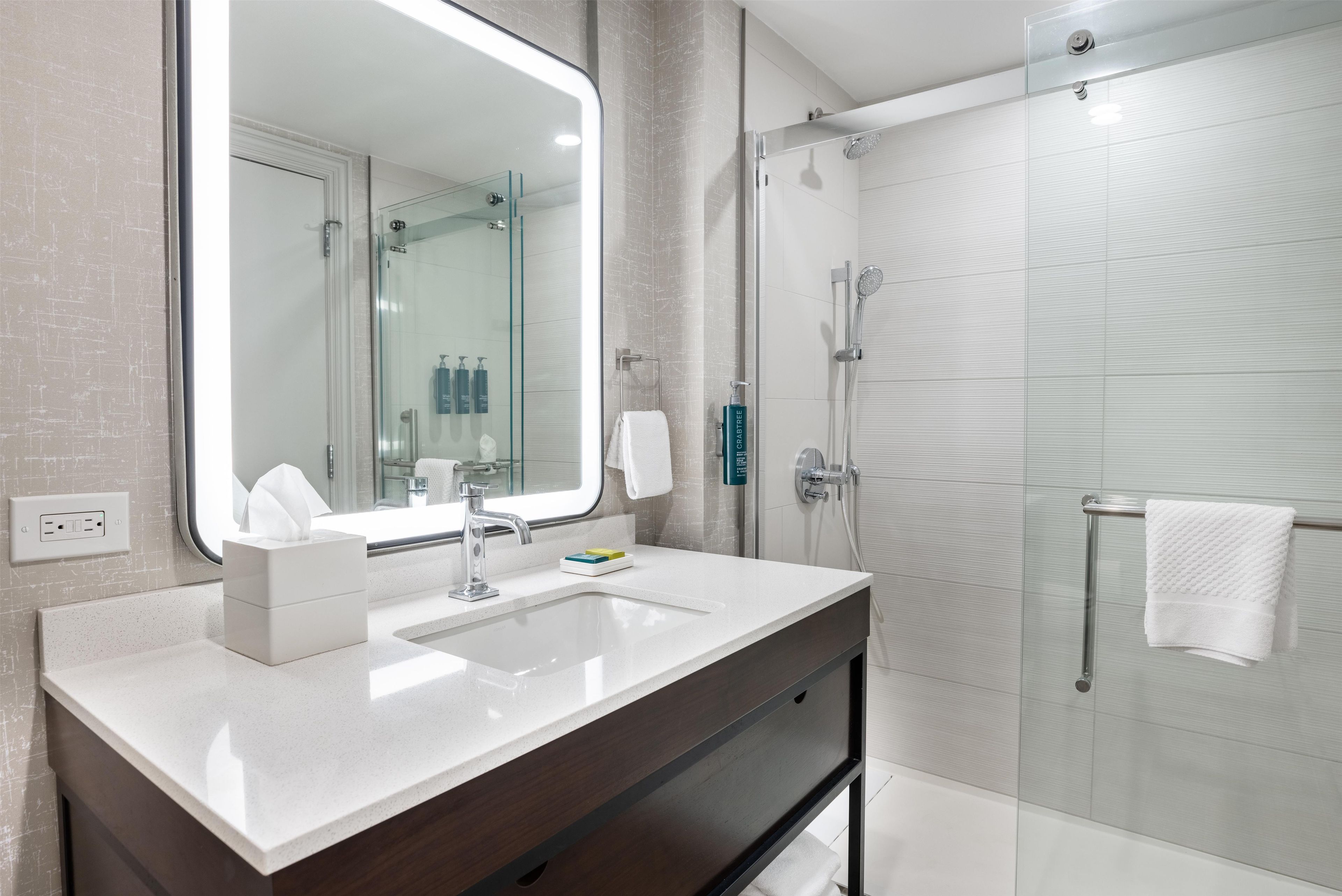 A modern bathroom with a large mirror, a sink, a shower, and a towel rack.