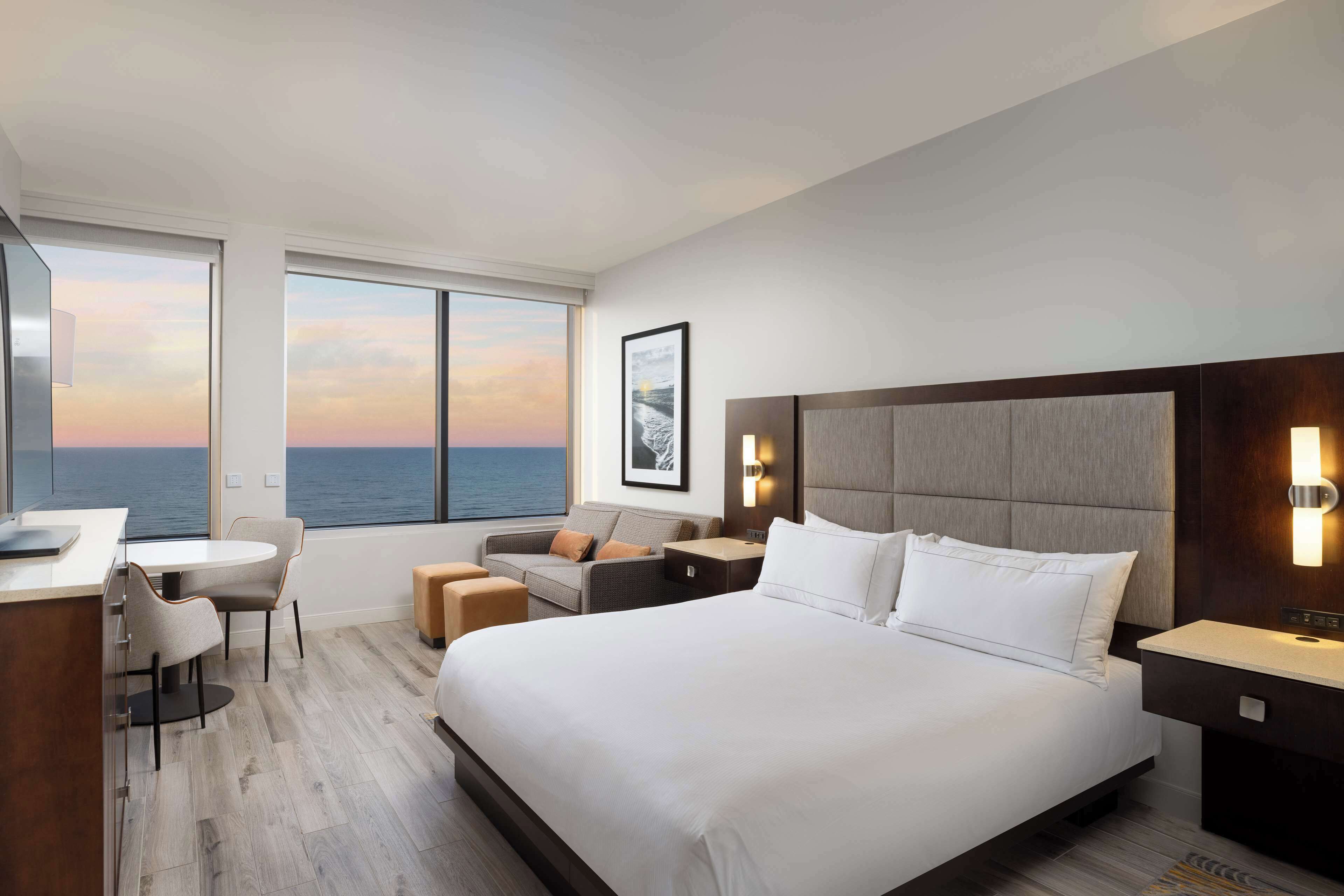 Ein modernes Hotelzimmer mit einem großen Bett, einem Schreibtisch, einer Couch und Meerblick.