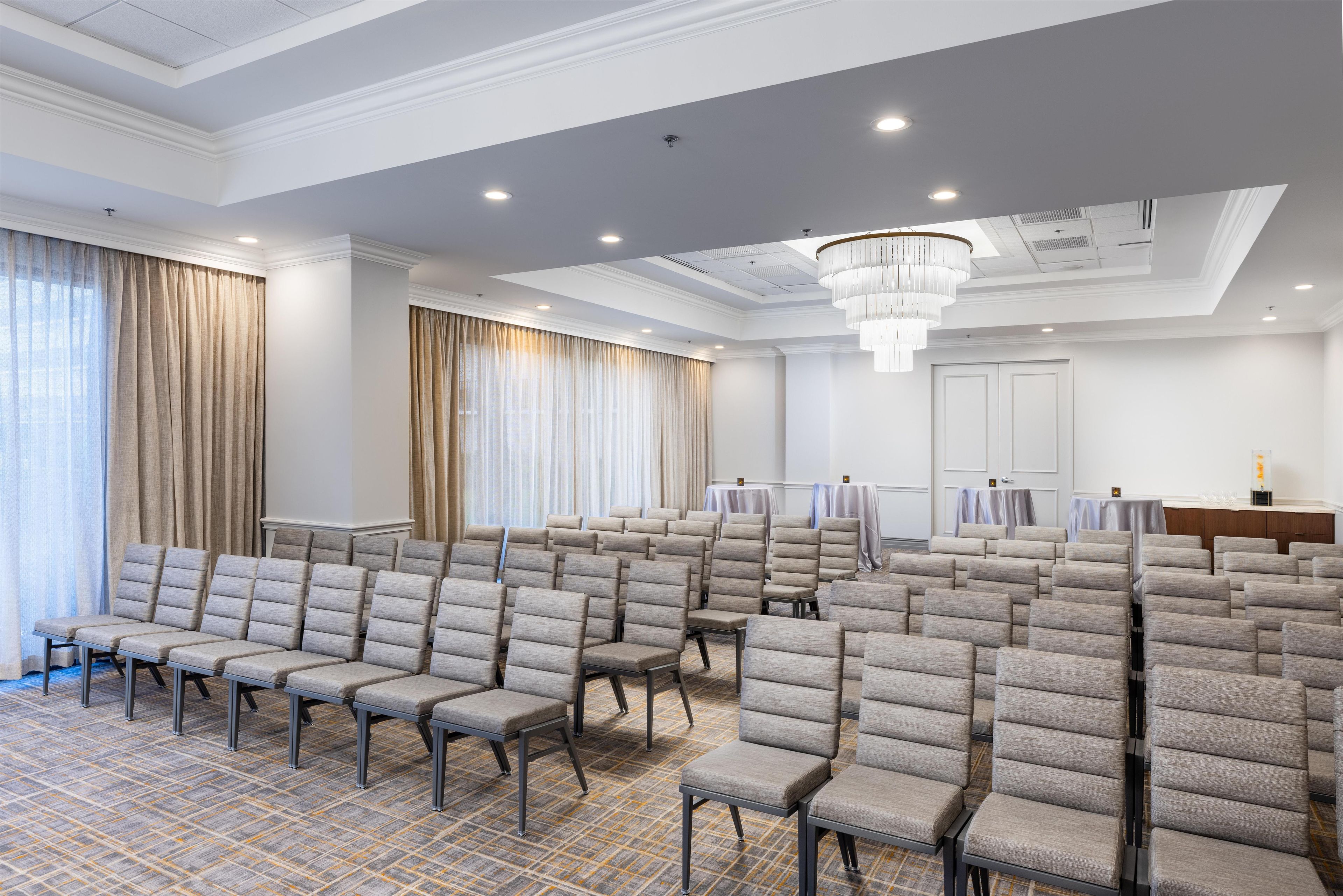 A conference room with rows of grey upholstered chairs, a patterned carpet, and a chandelier.