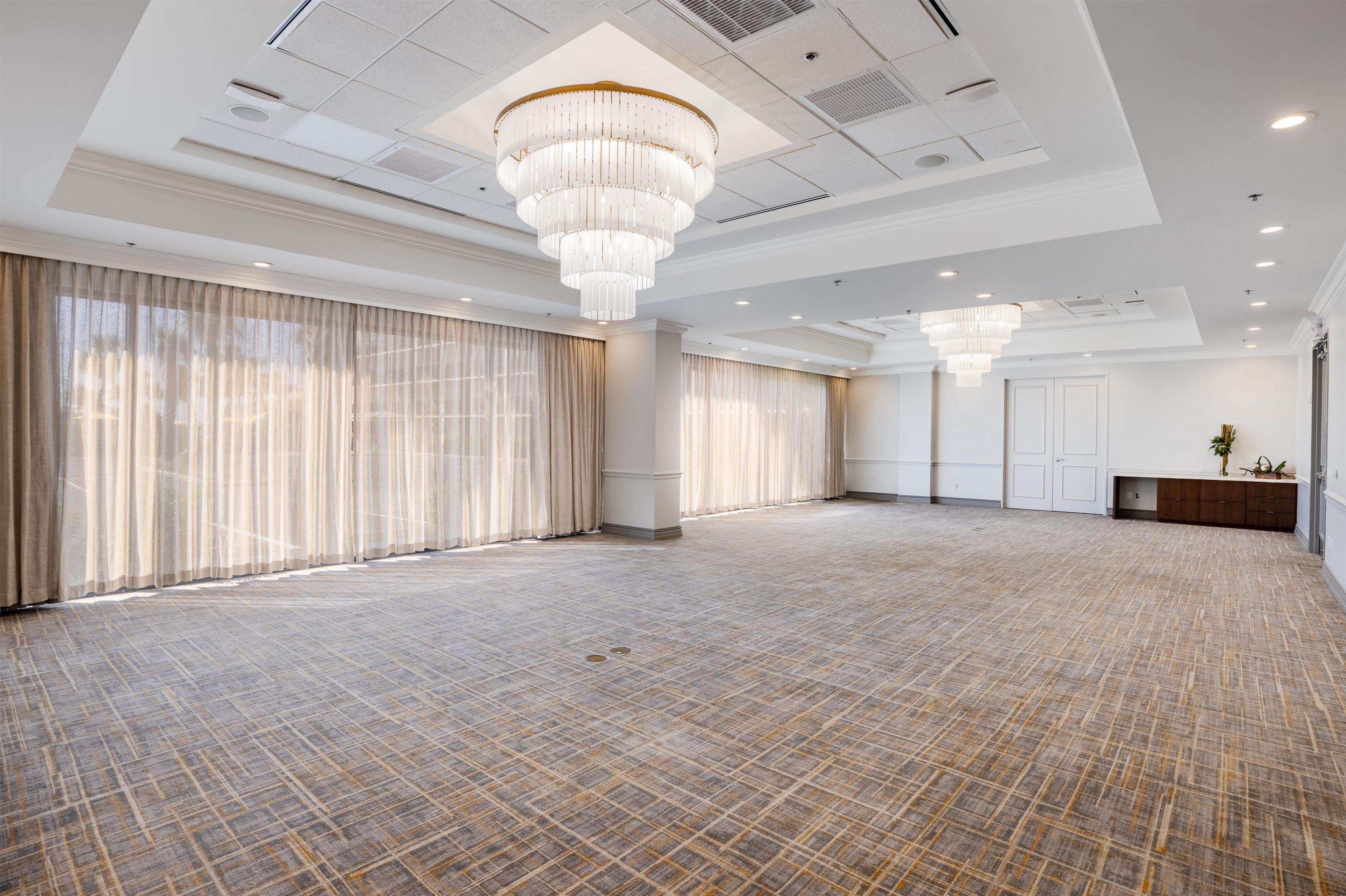 A spacious room with a patterned floor, large windows with curtains, and a chandelier.