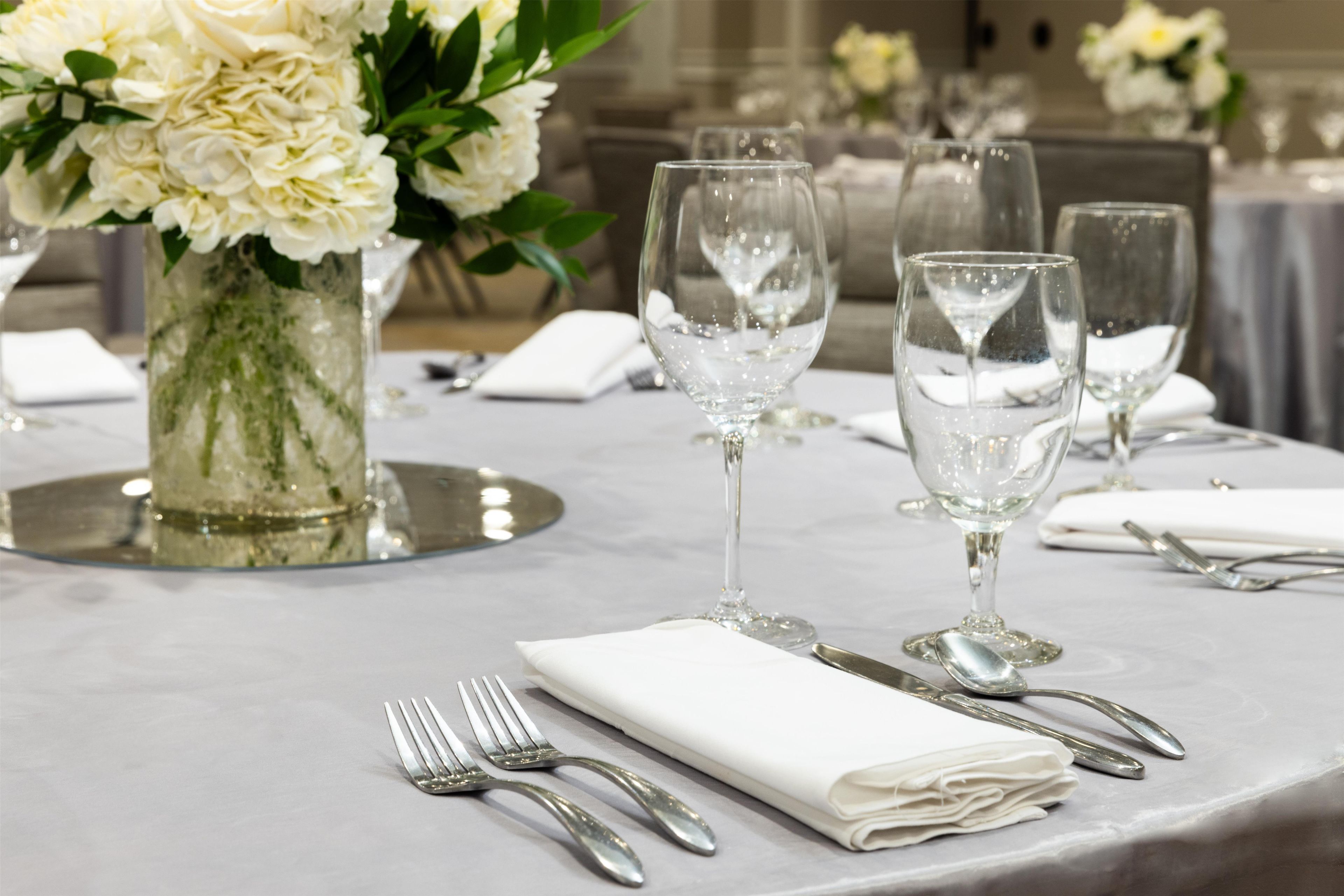 Una mesa lista para comer, con servilletas blancas, cubiertos y cristalería transparente.