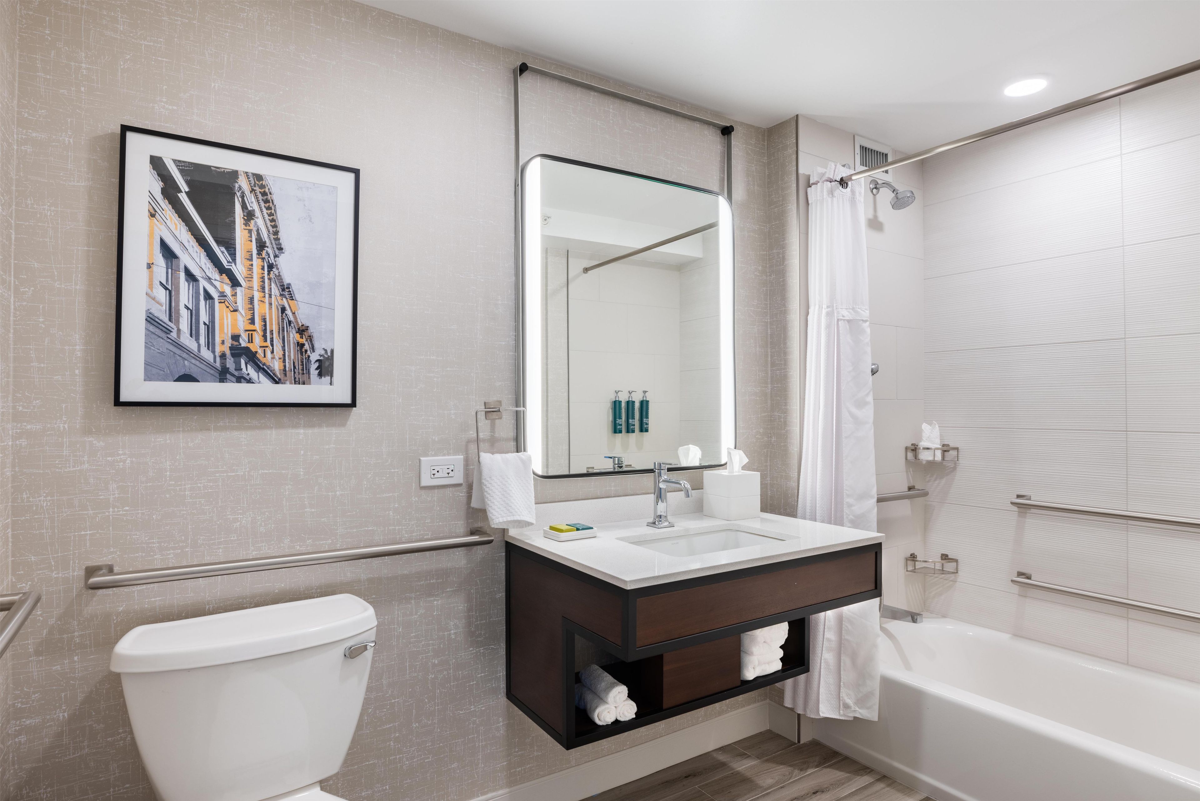 Un baño moderno con inodoro, lavamanos, espejo, ducha y un cuadro en la pared.
