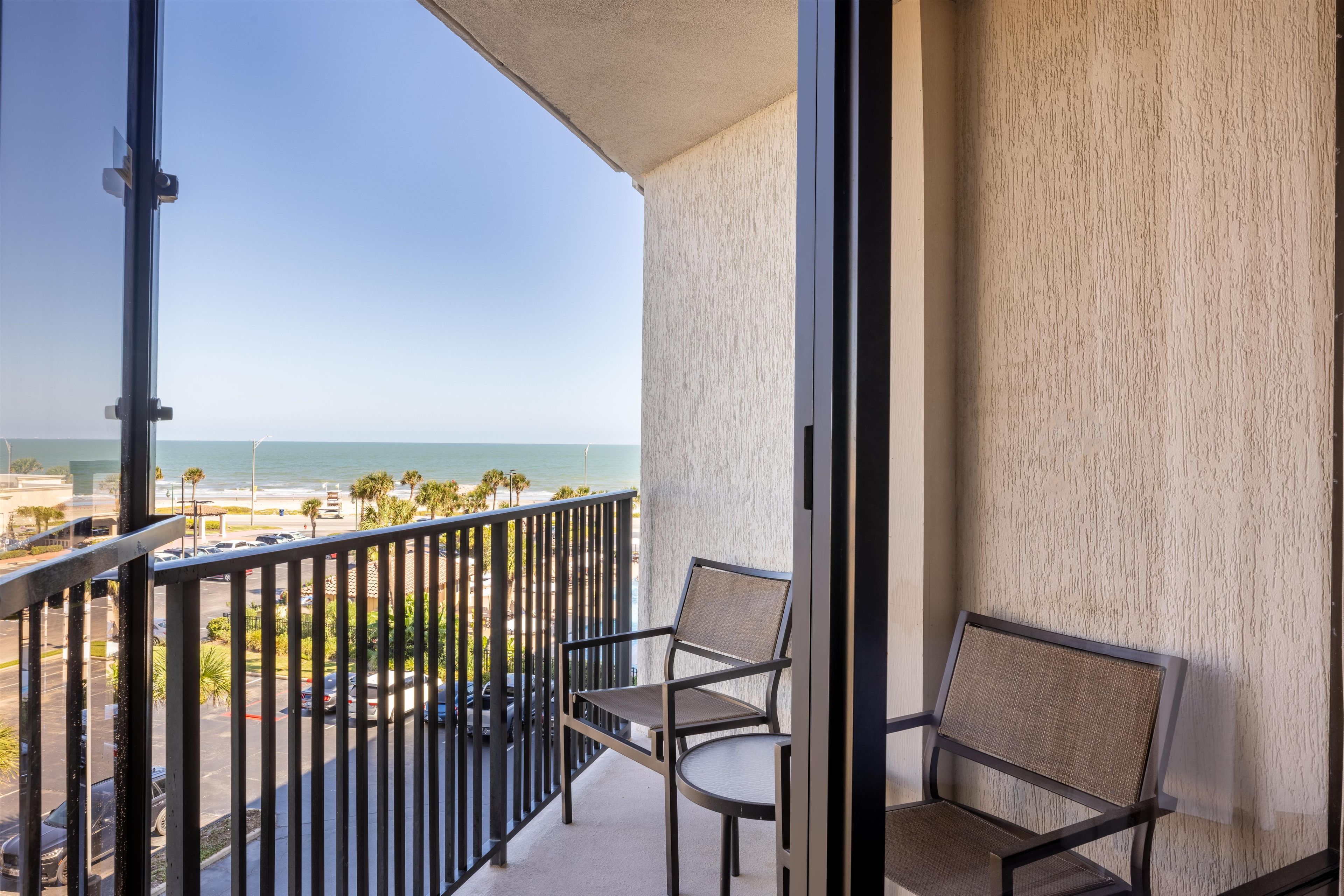 Un balcón con vista al océano y a la playa, con dos sillas y una mesa.