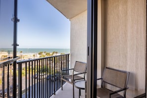 Een balkon met uitzicht op de oceaan en het strand, met twee stoelen en een tafel.