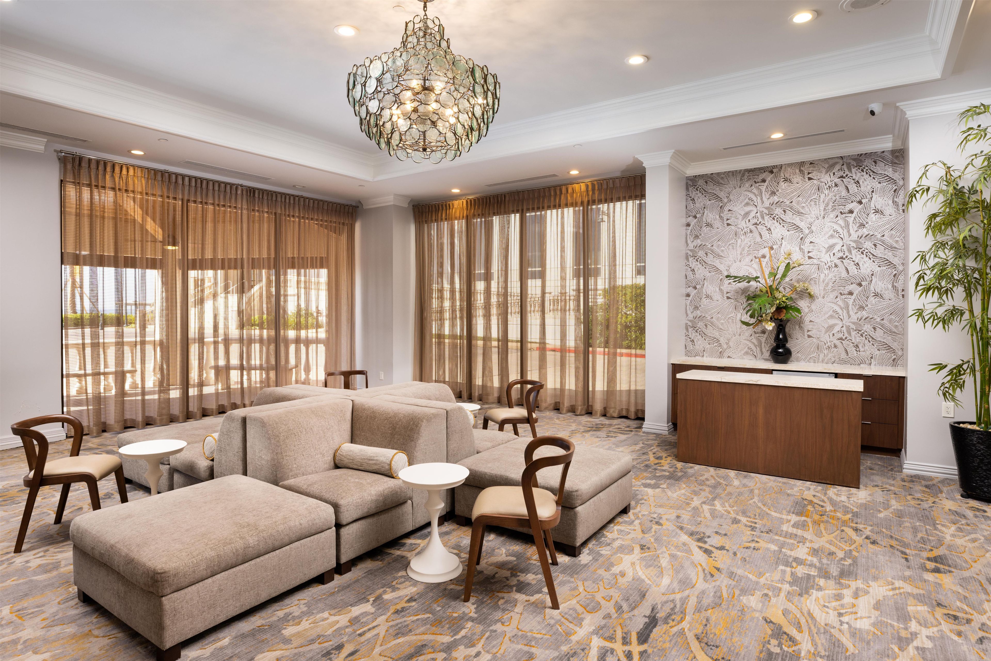 A hotel lobby with a sectional sofa, round tables, a reception desk, and a large window with curtains.