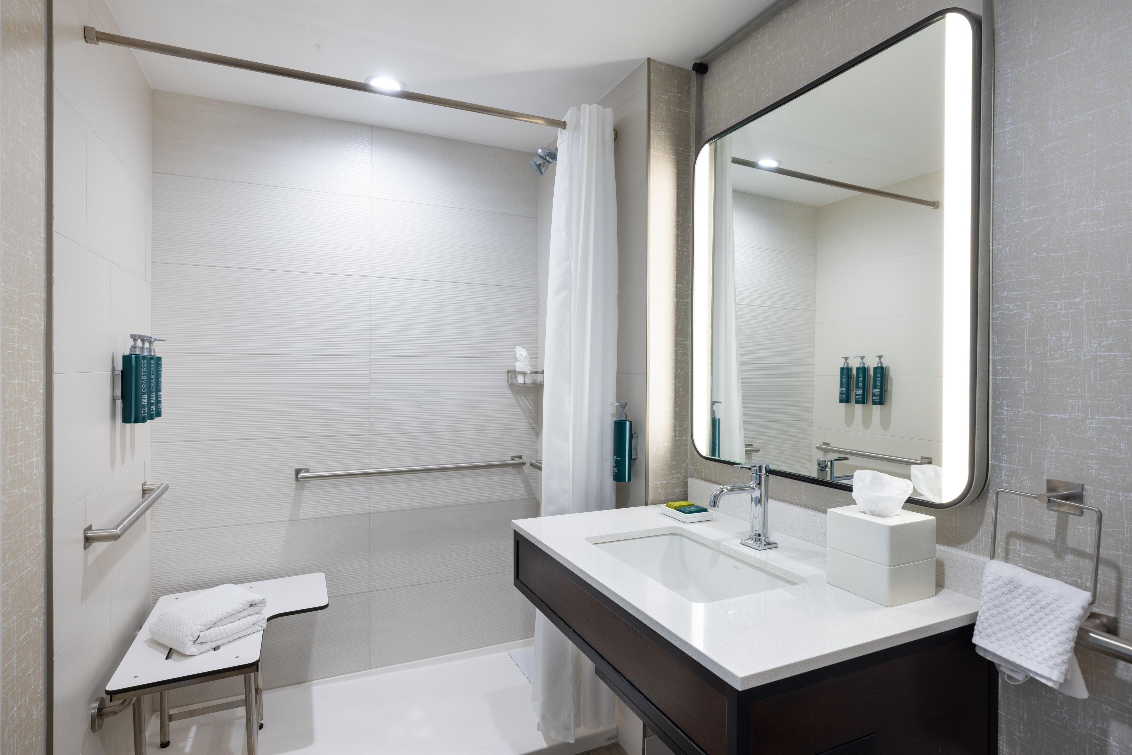 A modern bathroom with a white sink, a large mirror, and a shower area.