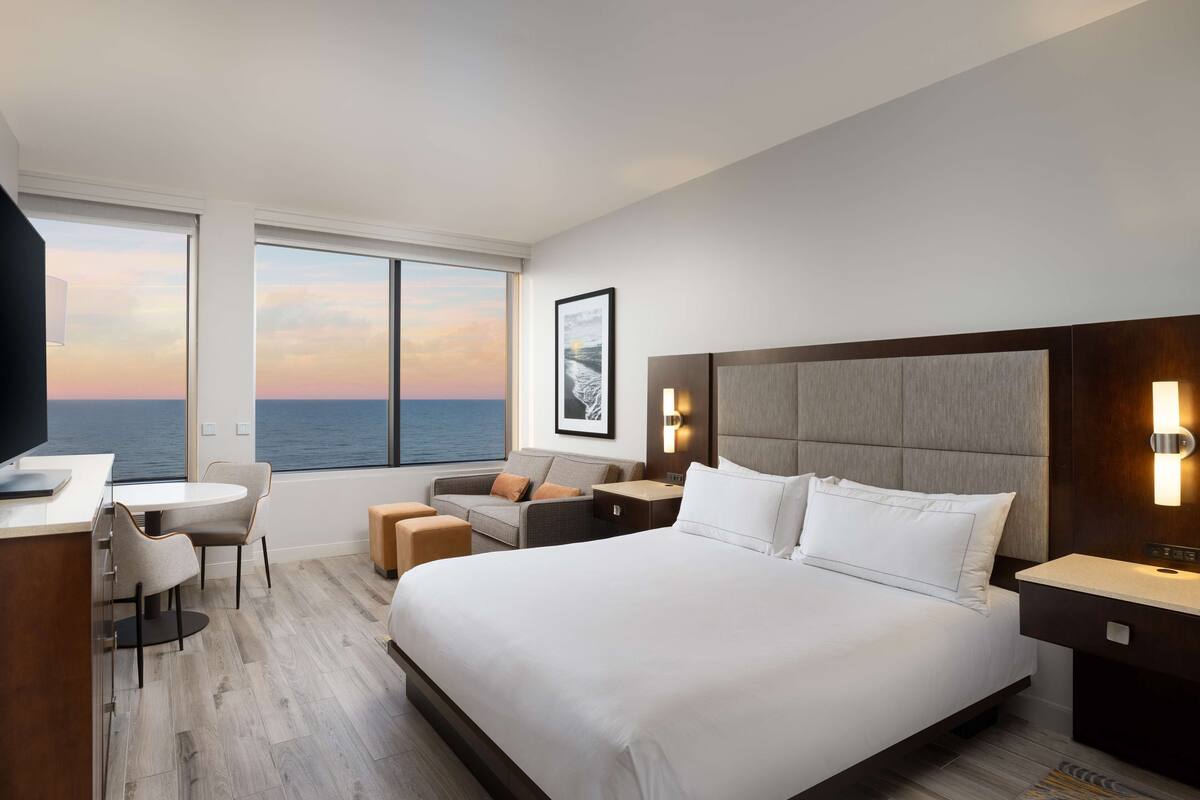 Een moderne hotelkamer met een groot bed, een bureau, een bank en uitzicht op zee.