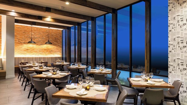 A restaurant with a brick wall, large windows, and neatly set tables.