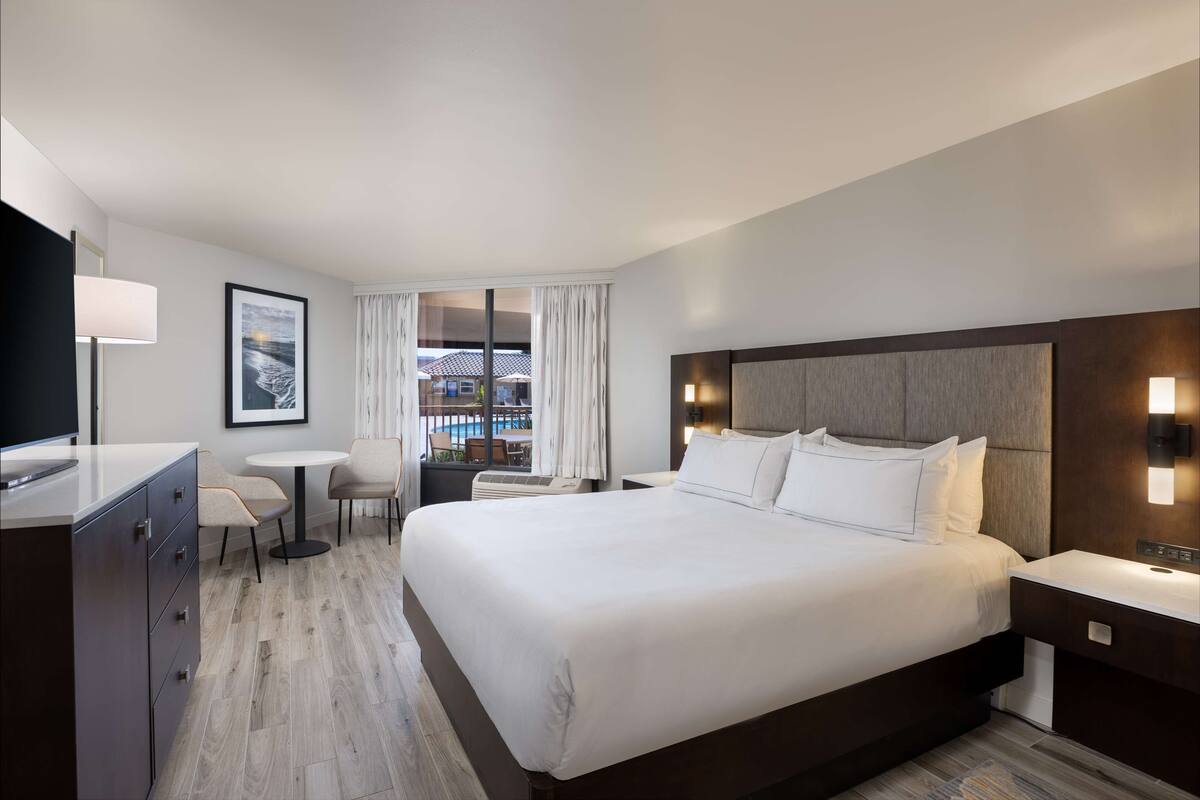 Een moderne hotelkamer met een groot bed, een bureau, een stoel, een kleine tafel en een raam met gordijnen.