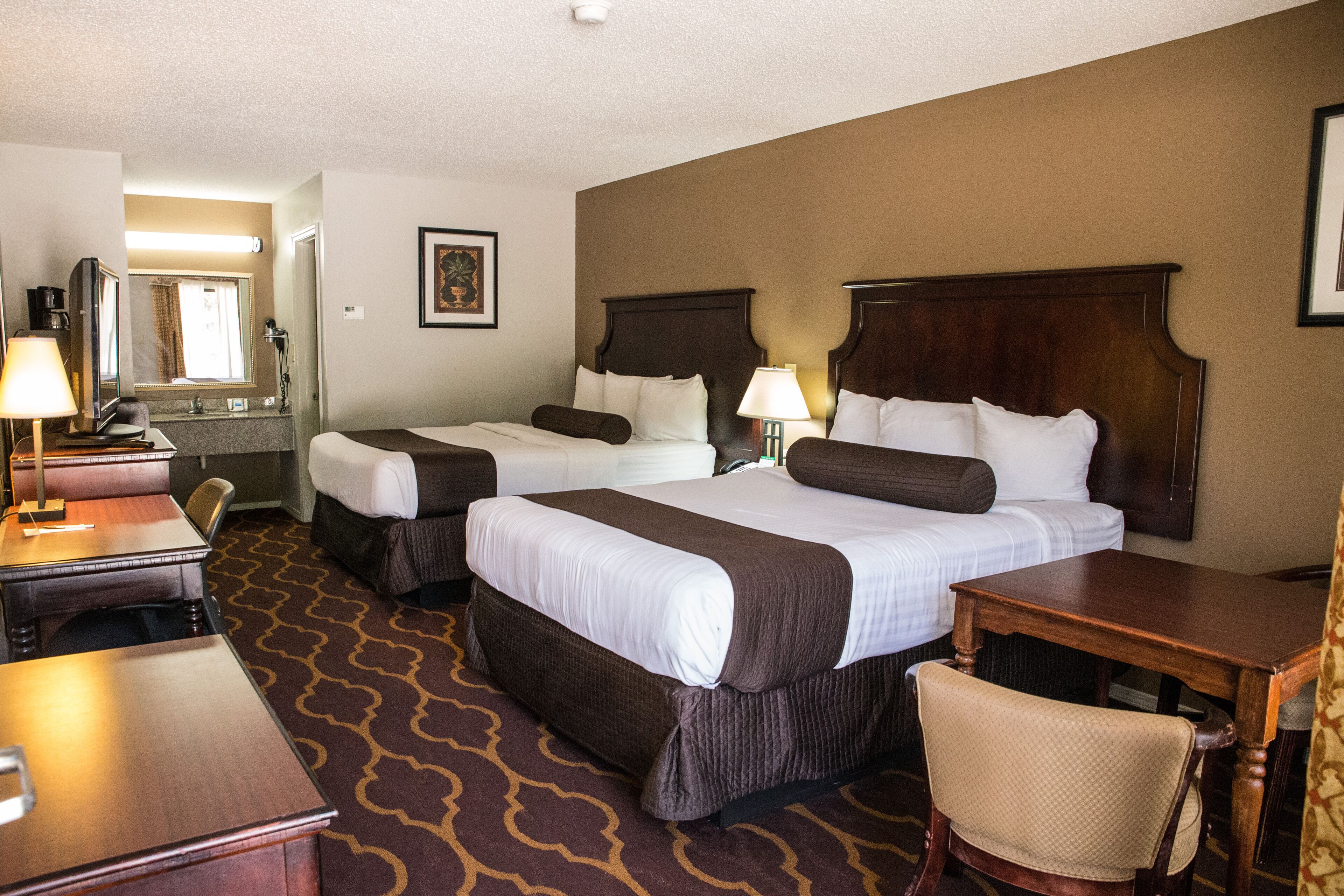 A hotel room with two beds, a desk, a chair, and a bathroom visible through an open door.