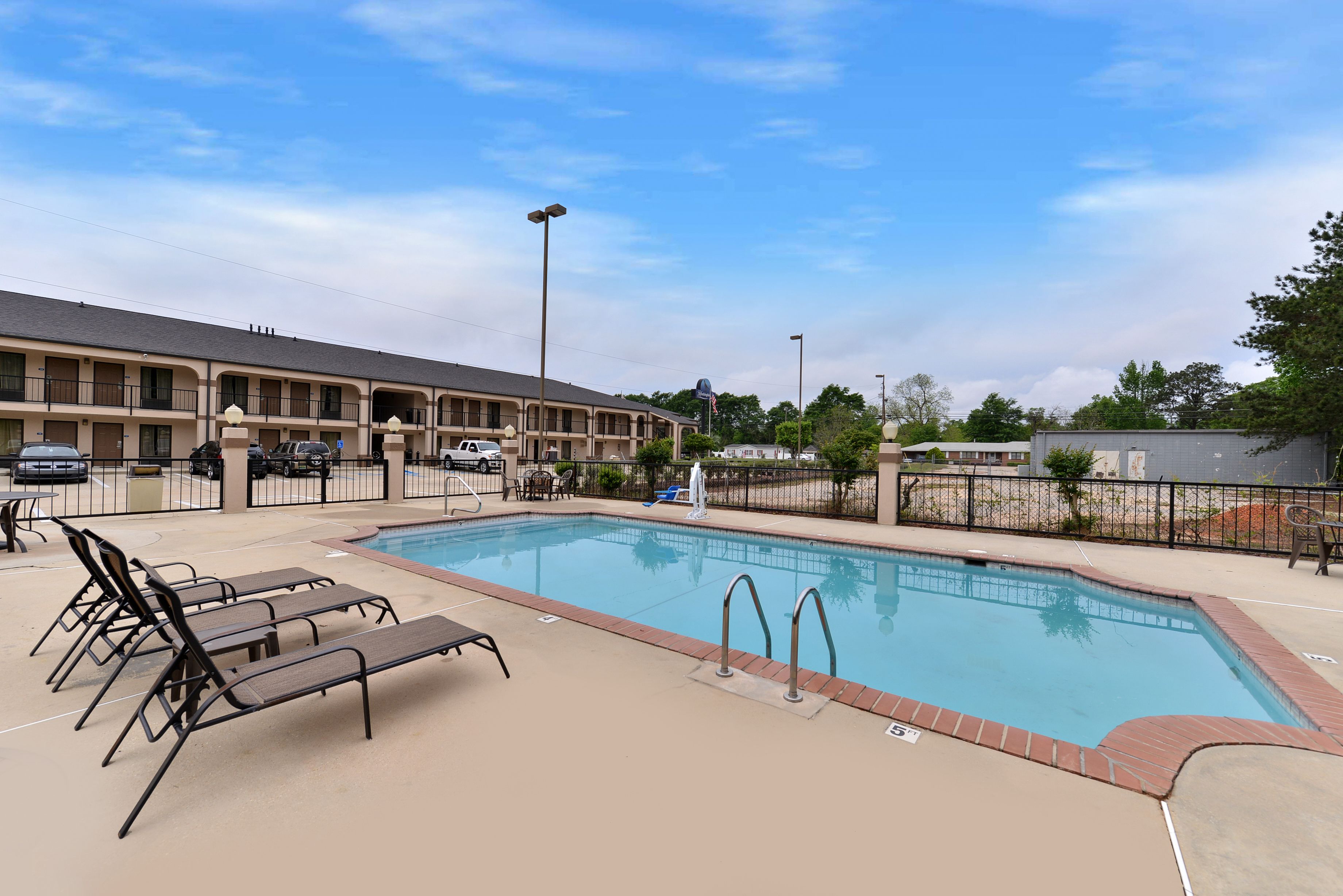 A hotel with a swimming pool, lounge chairs, and a parking lot.
