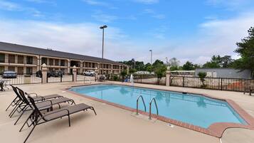 A hotel with a swimming pool, lounge chairs, and a parking lot.