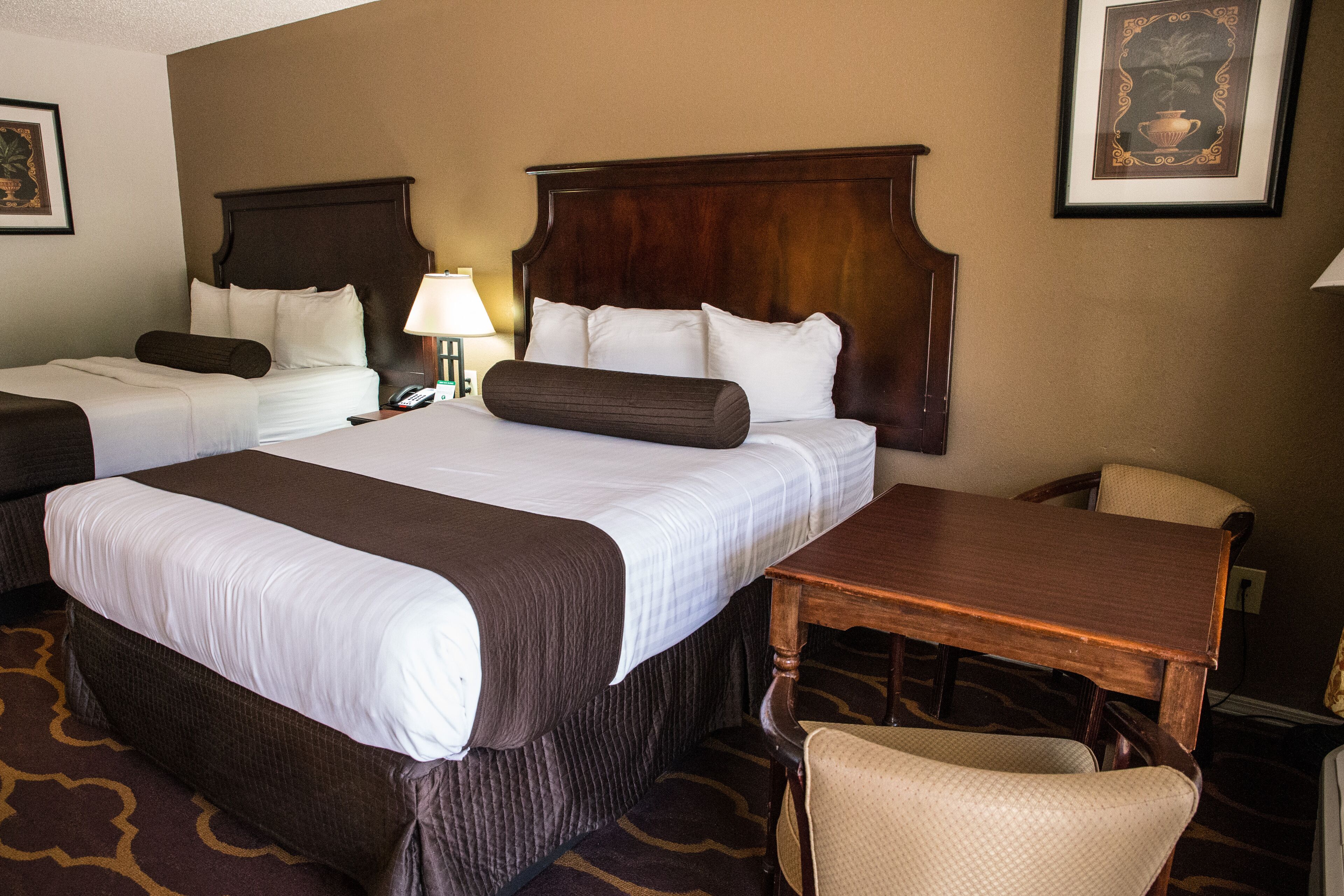 A hotel room with two beds, a wooden headboard, a desk, and a chair.