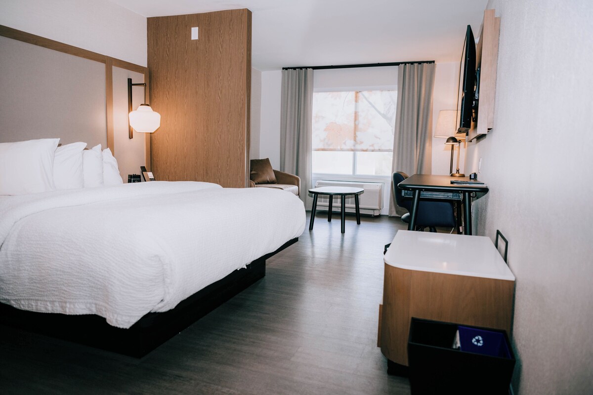 Habitación de hotel con una cama grande, un escritorio con silla, una mesita y un televisor fijado a la pared.