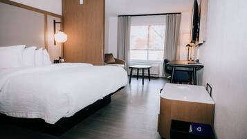 A hotel room with a large bed, a desk with a chair, a small table, and a TV mounted on the wall.