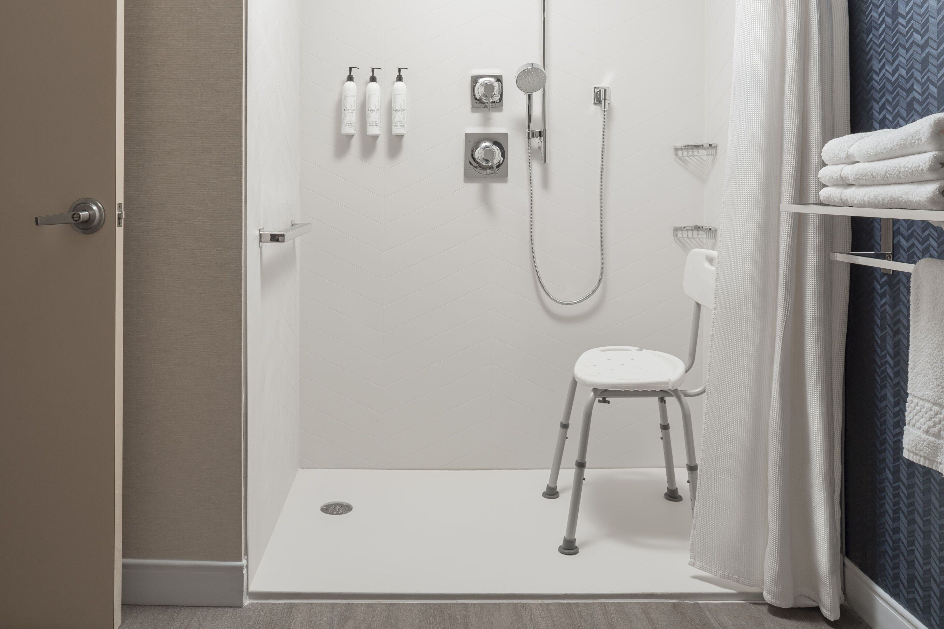 A modern bathroom with a walk-in shower, a white toilet, a small stool, and a towel rack with folded towels.