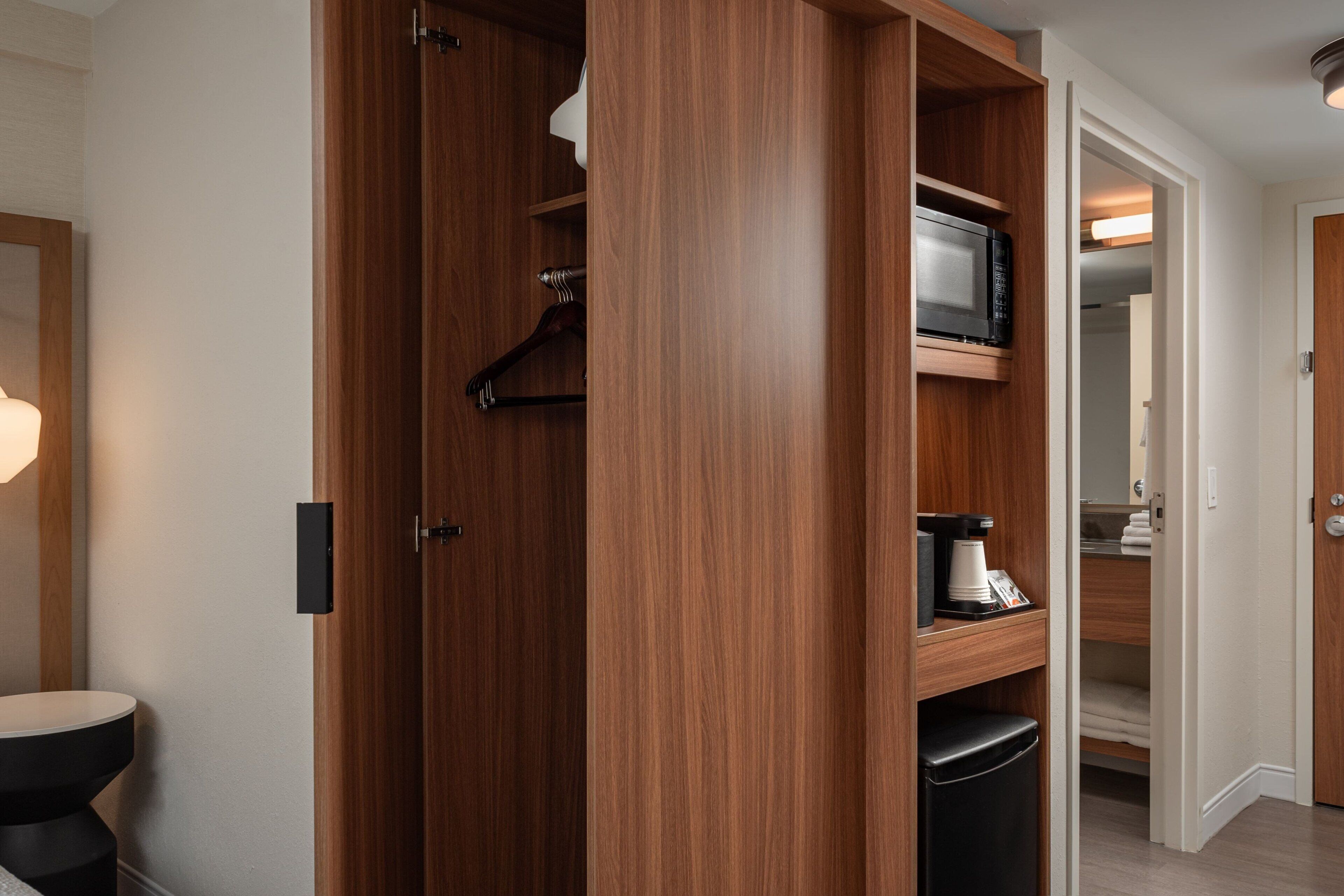 A wooden closet with a microwave, a coffee maker, and a hanging rack.